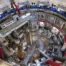 Vedere aeriană fisheye a interiorului halei tokamak ITER în etapa de asamblare, cu platforma circulară, structuri metalice, eșafodaj și conducte de ventilație roșii — șantierul de construcție al celui mai mare reactor de fuziune nucleară din lume
